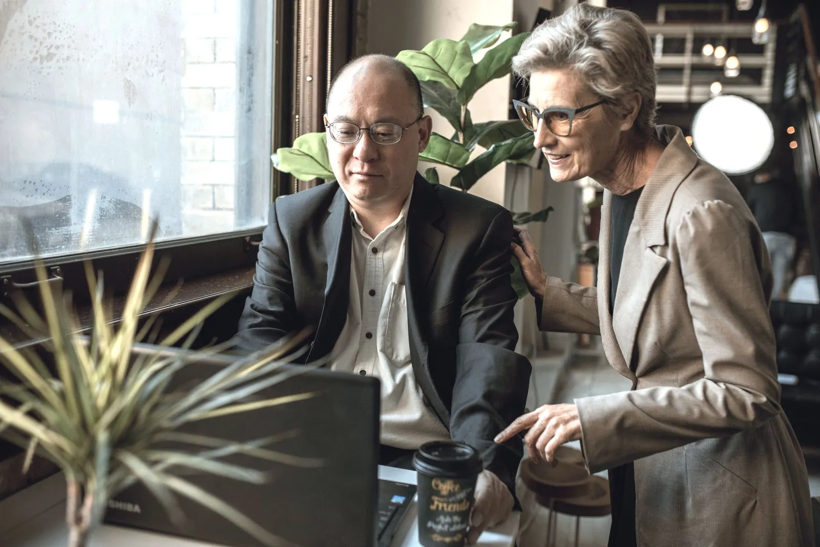 A senior colleague leans in to talk a point through at a laptop.