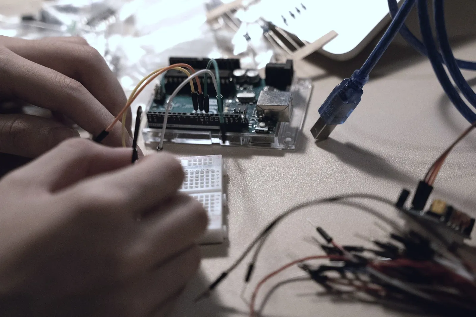 Hands wire a small electronic board at a wooden desk.
