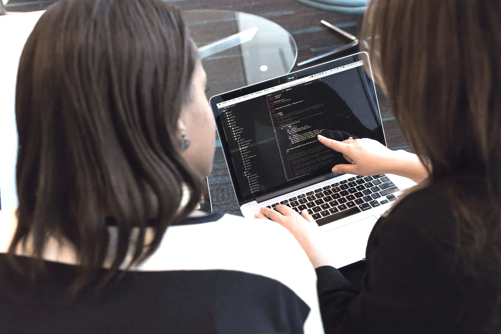 Two colleagues look at code on a laptop together.