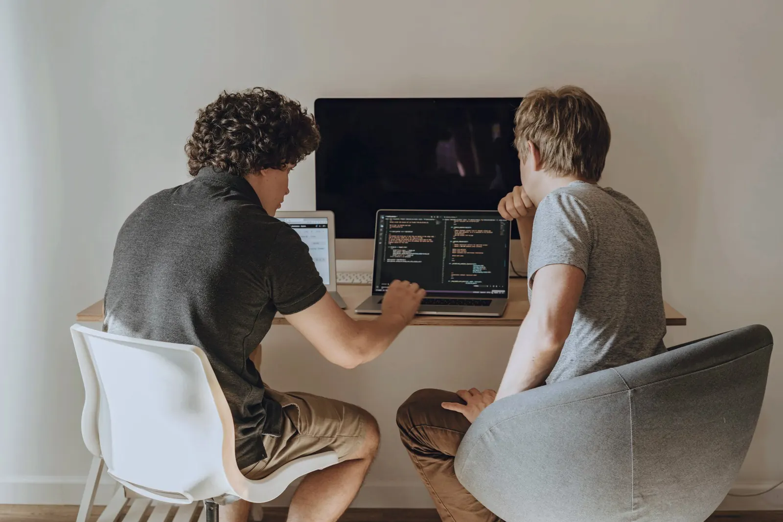 Two colleagues talk through code at a shared desk in warm light.