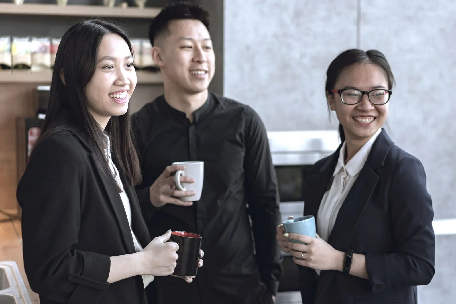 Three coworkers smile with mugs in hand during a break.