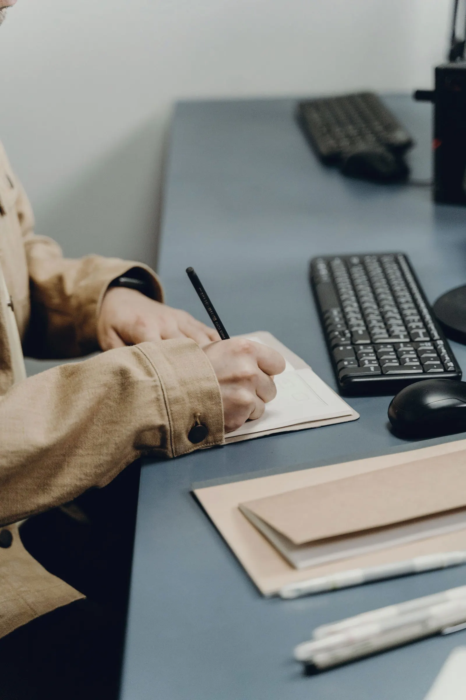 A colleague takes notes in a notebook at a desk with a keyboard.