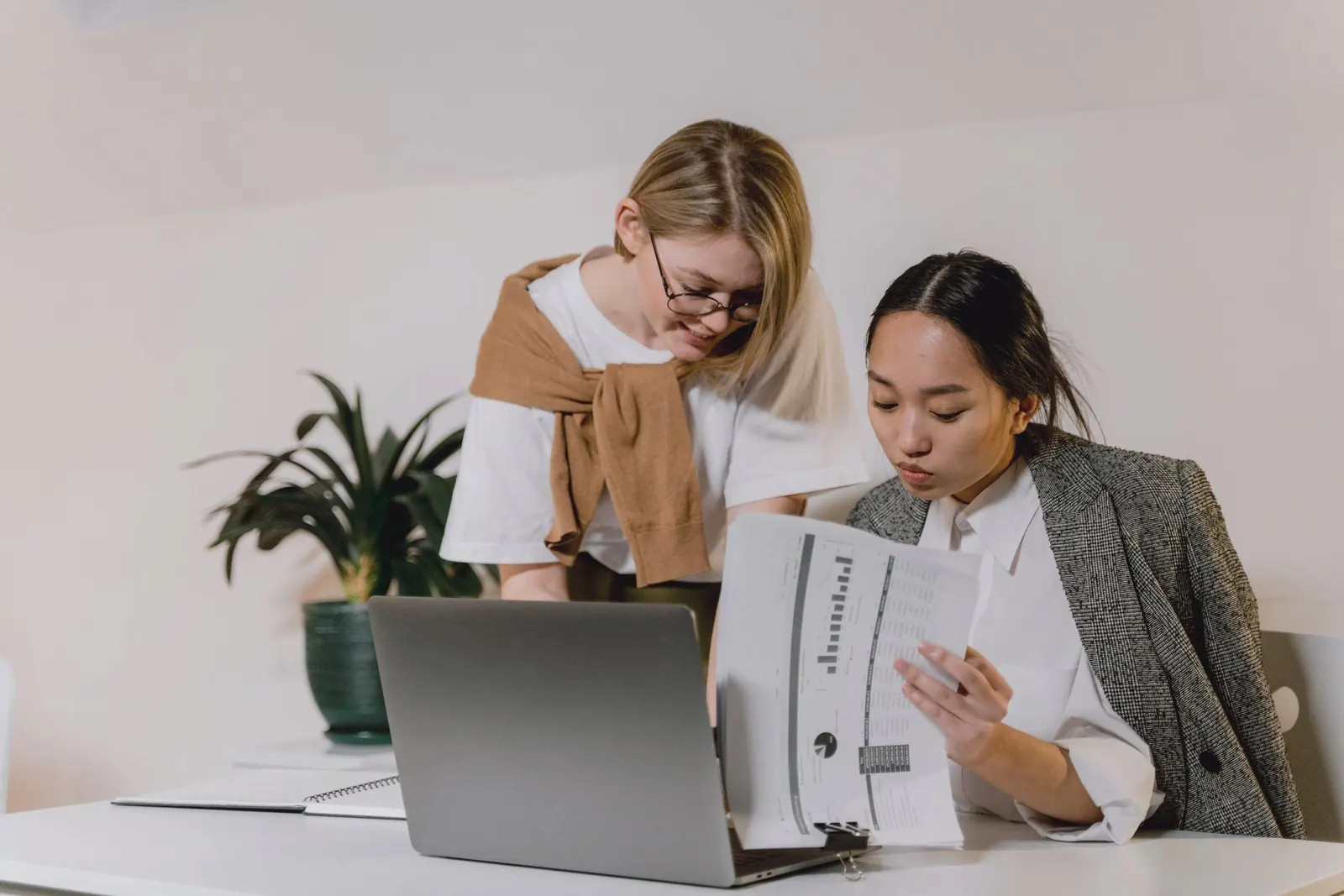 Two colleagues review a binder of findings beside a laptop.