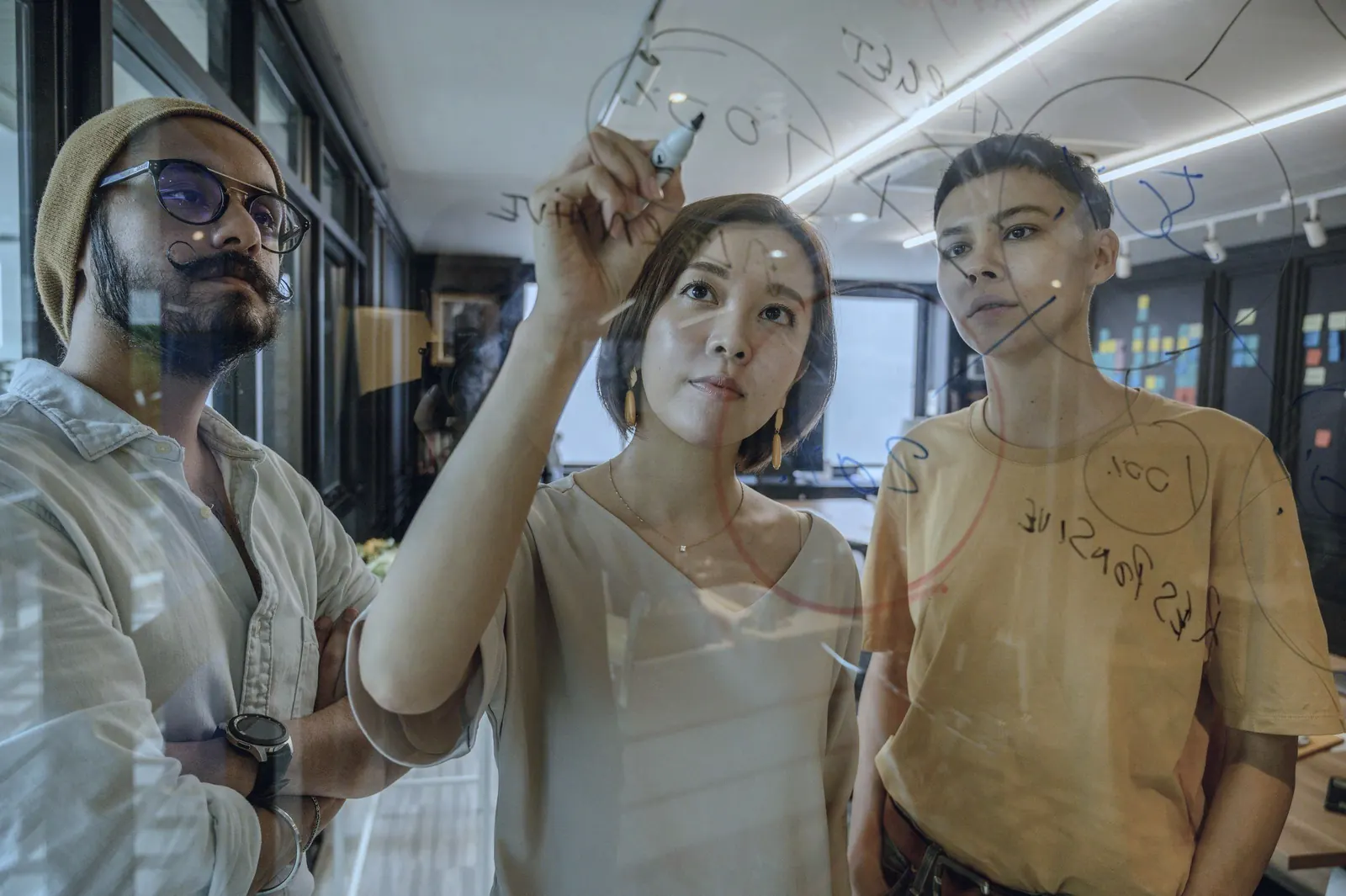 Three colleagues sketch ideas together on a glass wall.
