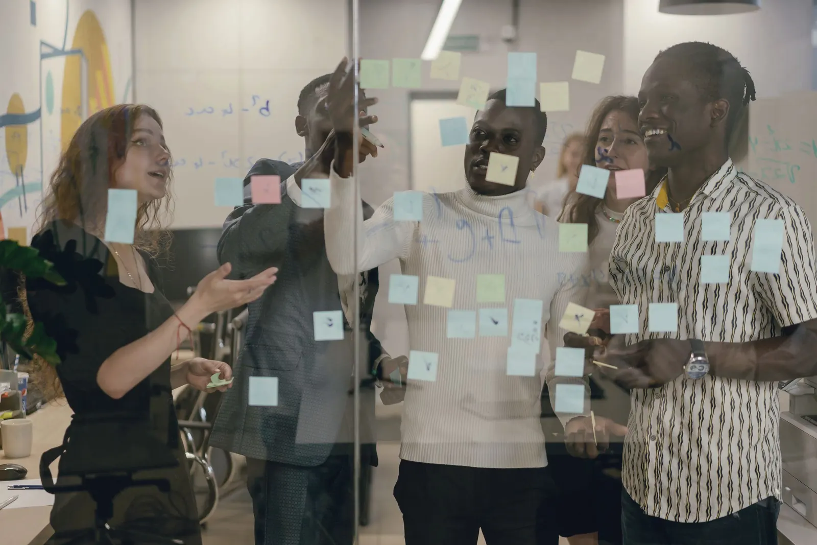 A team sorts sticky notes on a glass wall, seen through the glass.