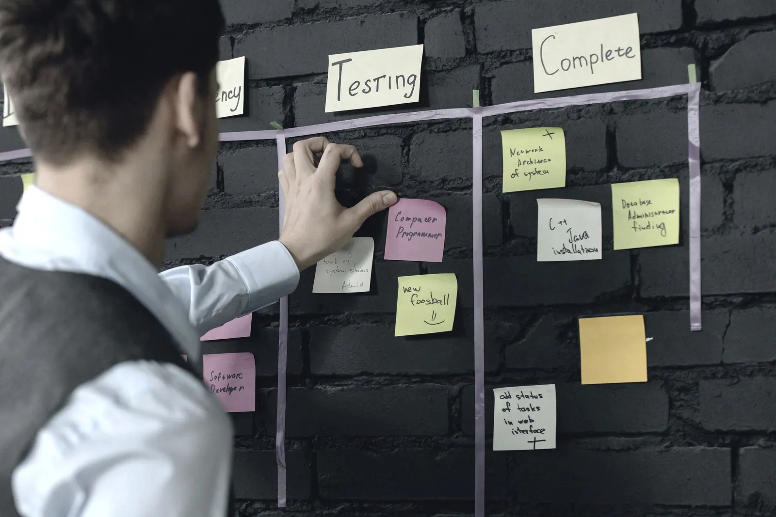 A colleague moves a note on a wall of tasks in a brick-walled office.