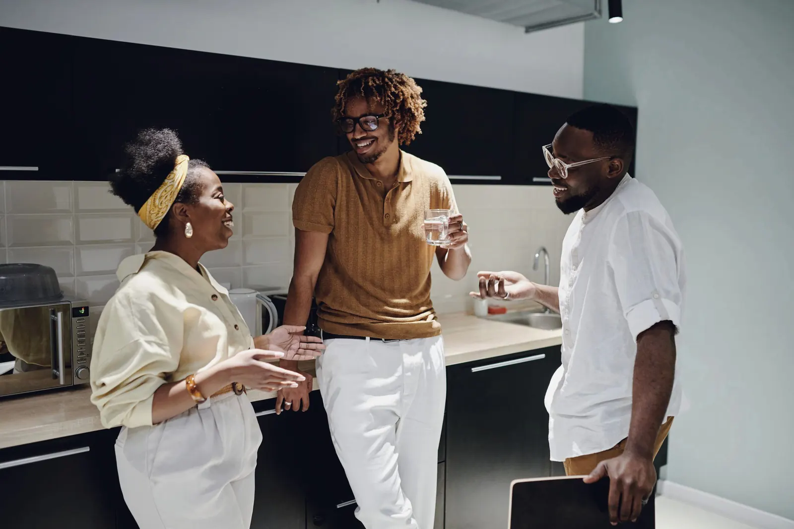 Three colleagues laugh together in an office kitchen.