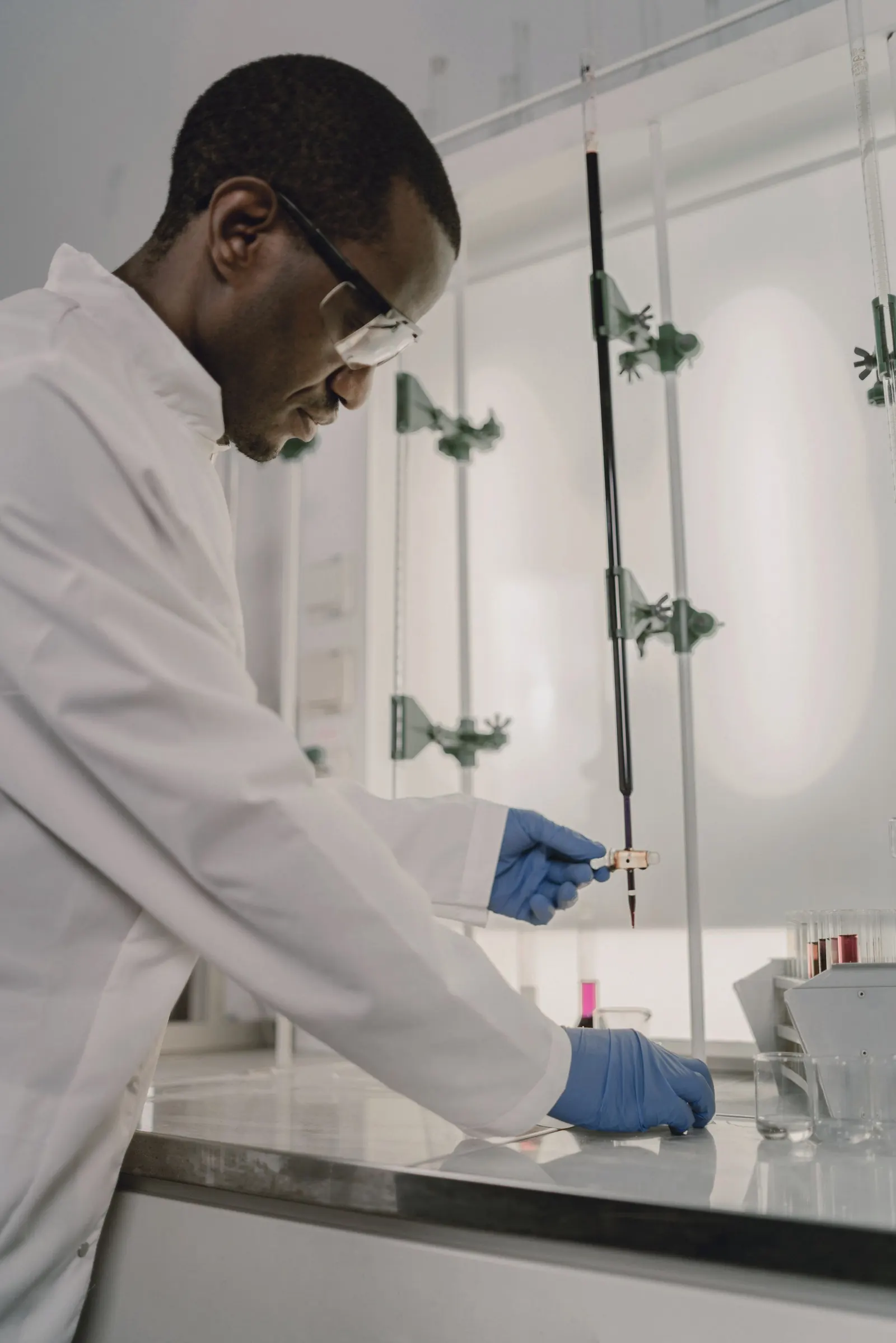 A chemist in safety glasses works at a laboratory bench.