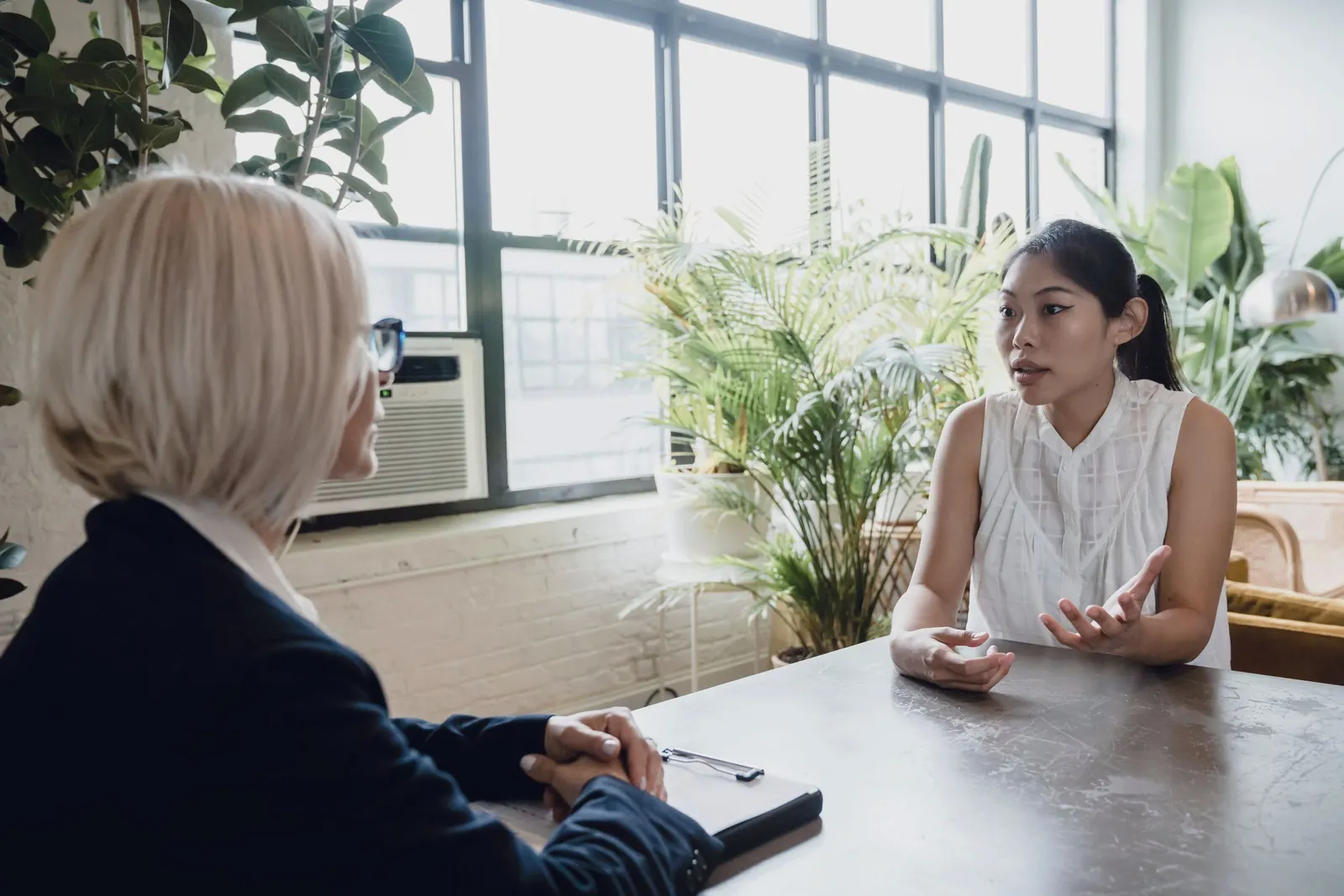 Two colleagues talk across a table in a bright office, one listening closely.