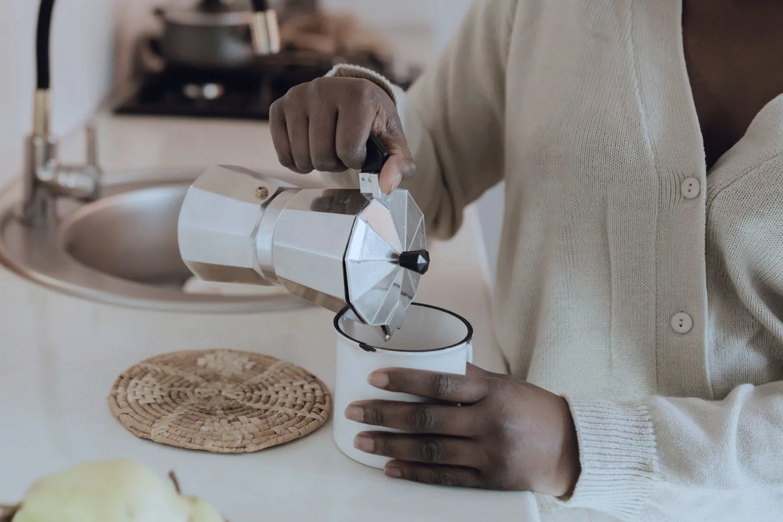 A hand pours coffee from a moka pot into a mug.