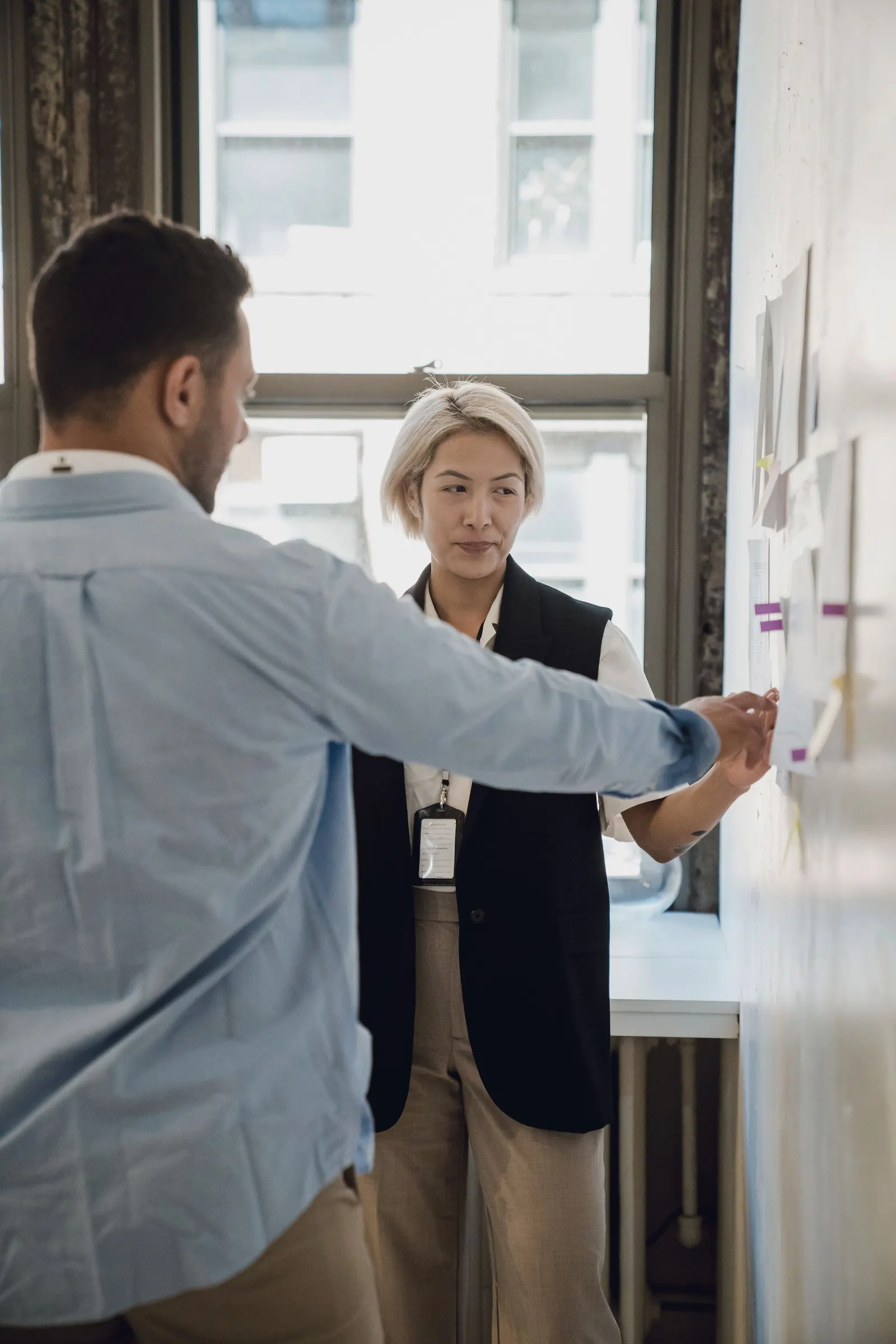 Two colleagues review notes pinned to a wall.