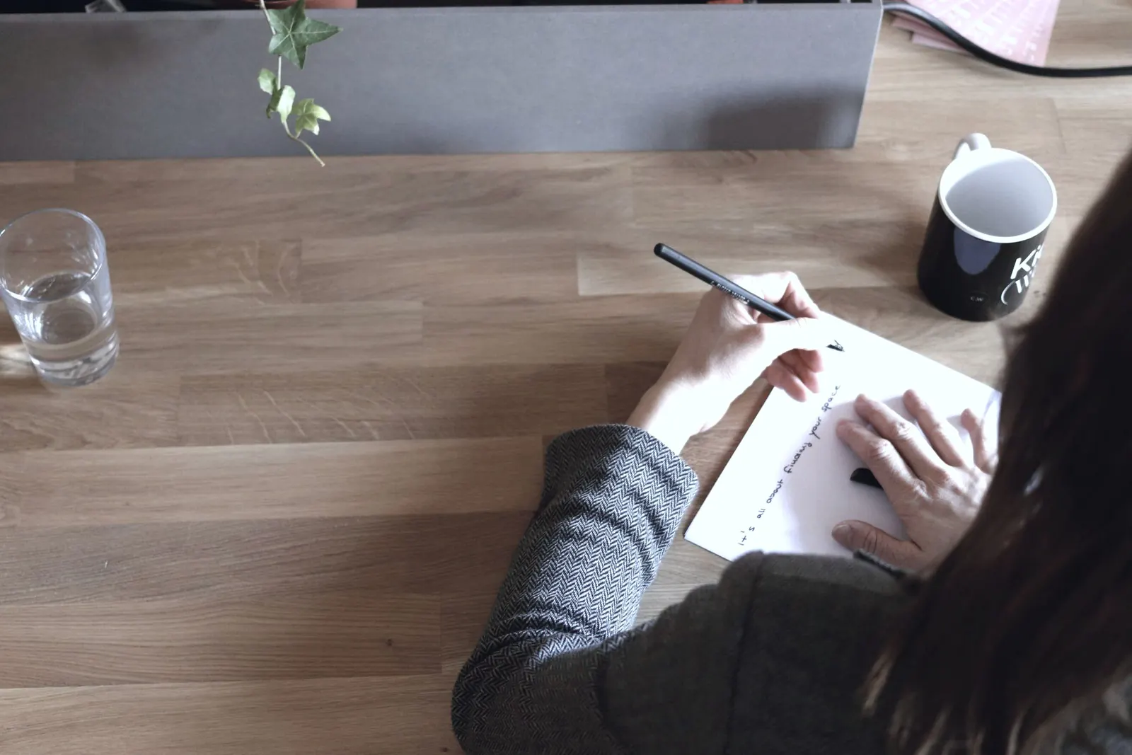 A colleague takes notes on paper at a wooden desk.