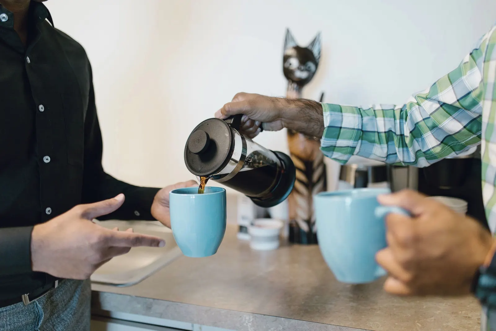 Hands pour fresh coffee into blue mugs during an office break.