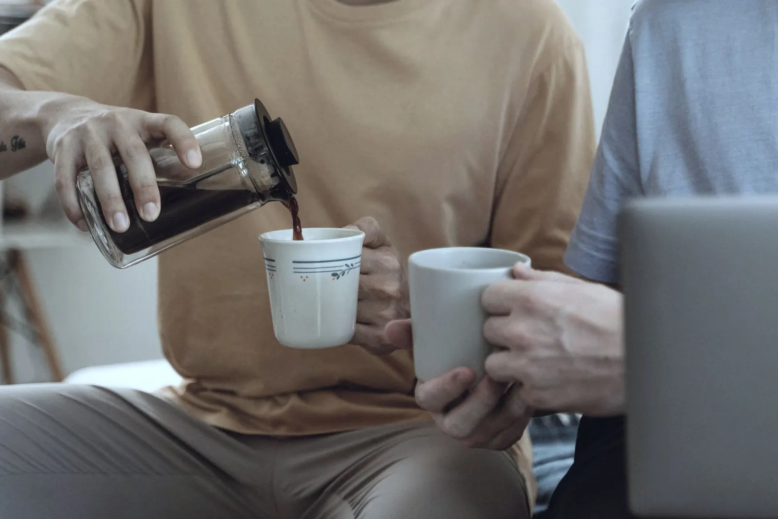 Coffee is poured from a press into mugs held by two colleagues.