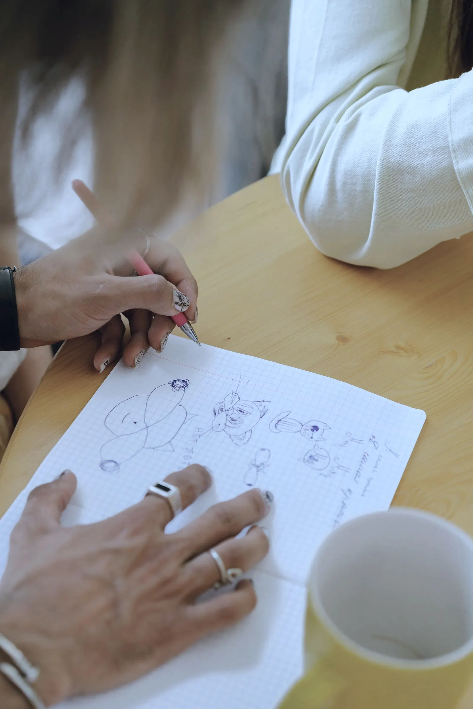Hands sketch a diagram on paper beside a yellow mug.
