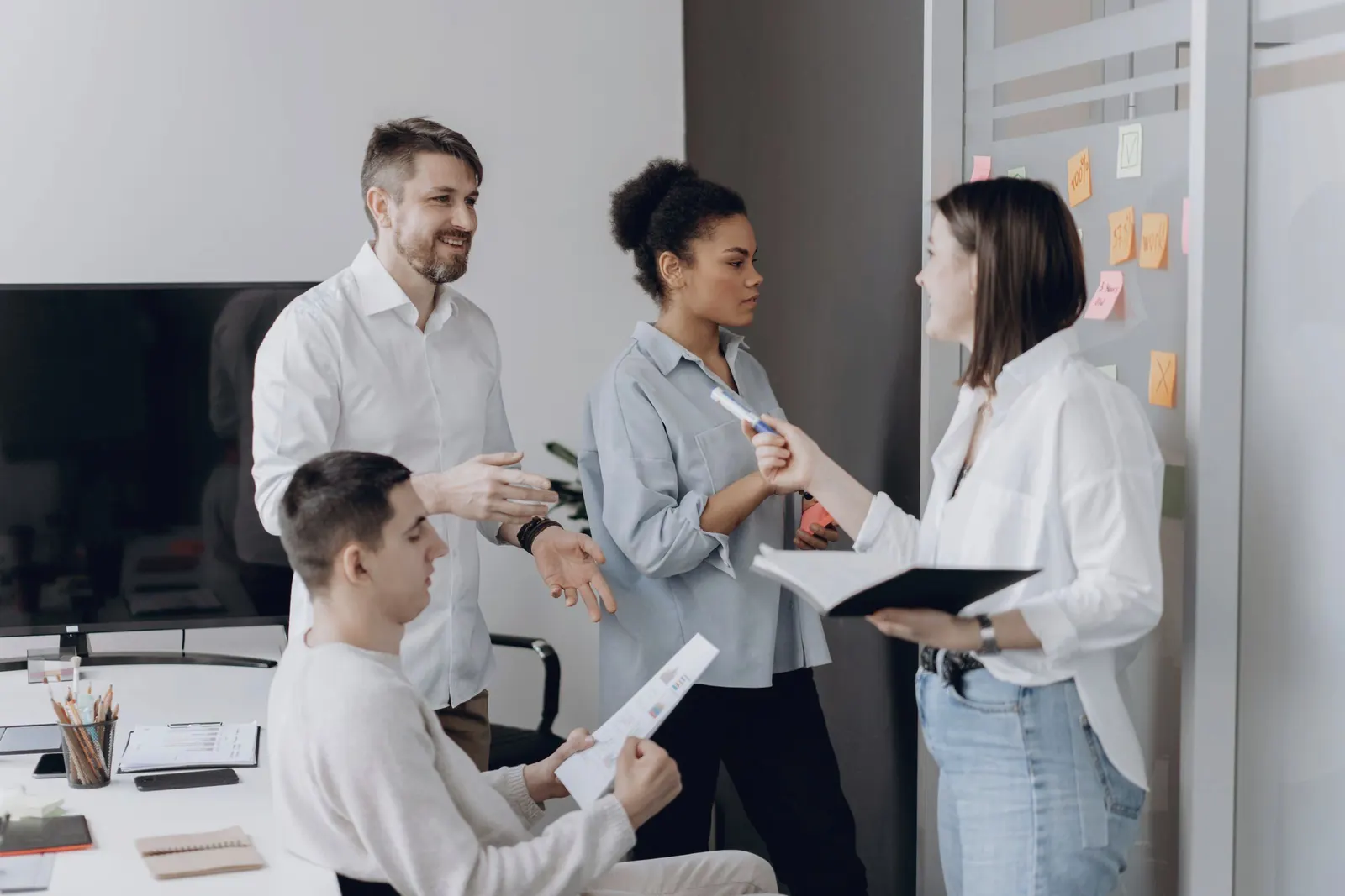 A small team stands together and talks through the day, notebooks in hand.