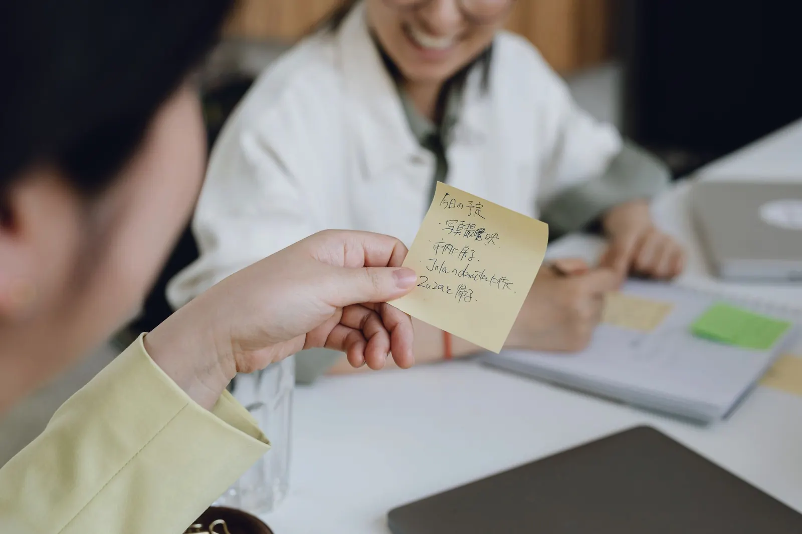 A hand holds up a written note as colleagues smile across the table.