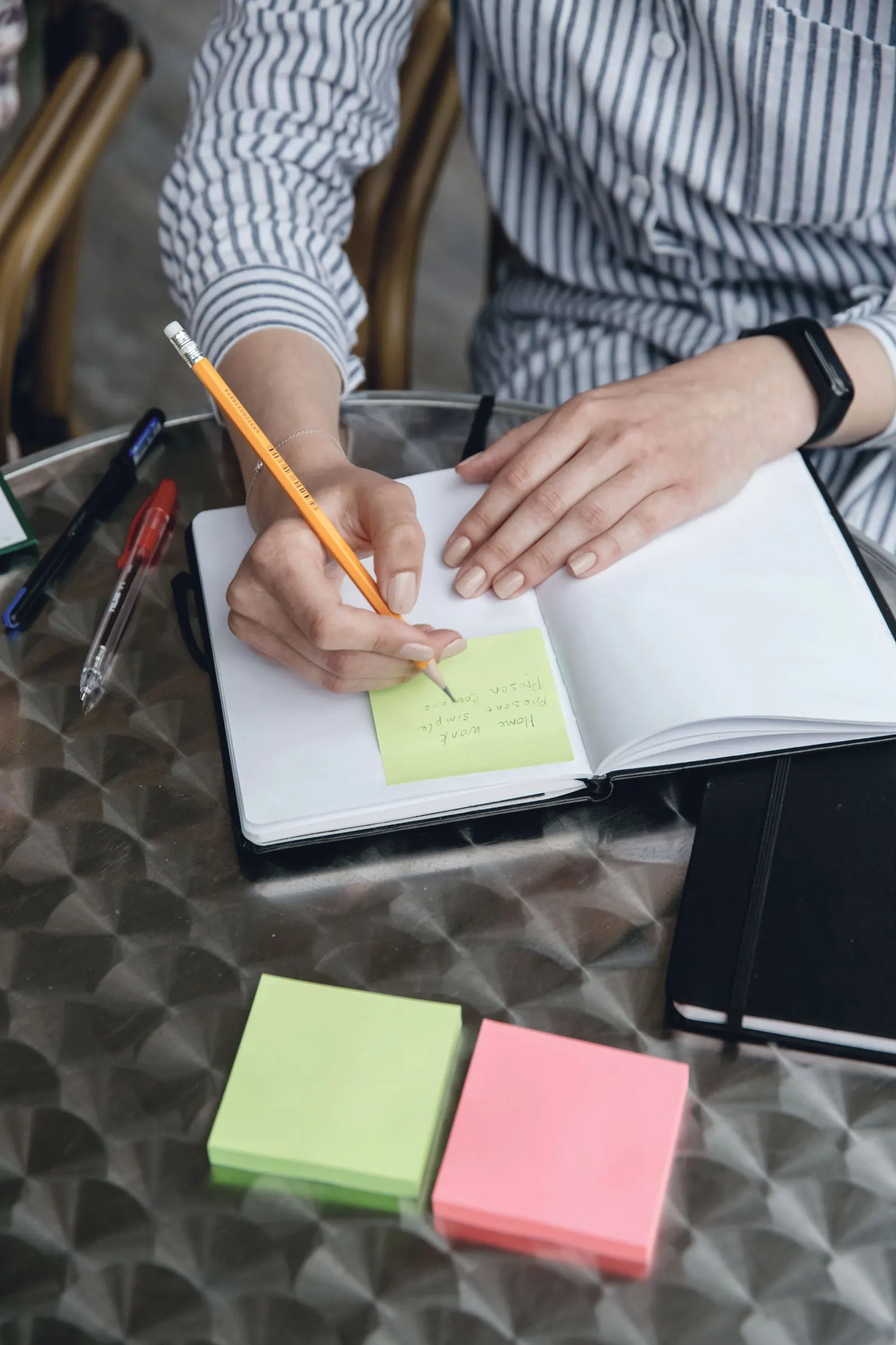 A hand writes on a sticky note beside an open notebook.