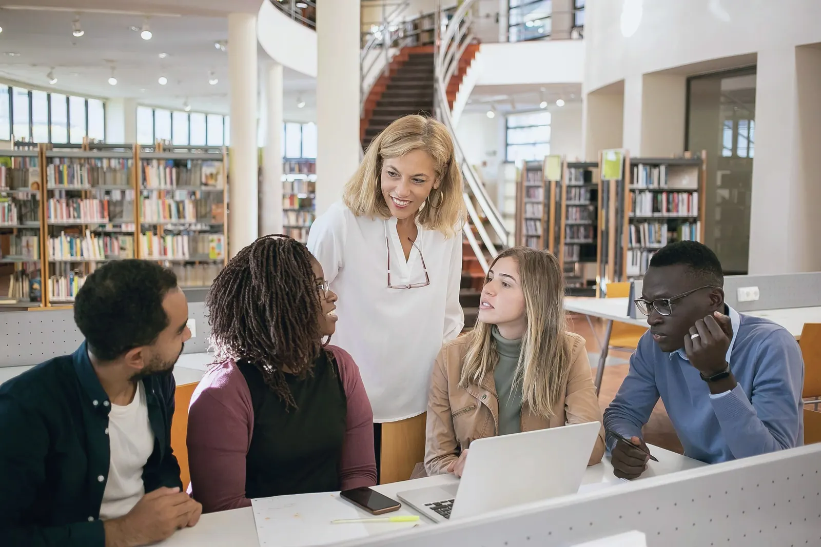 Students and a professor study together around a table with a laptop.