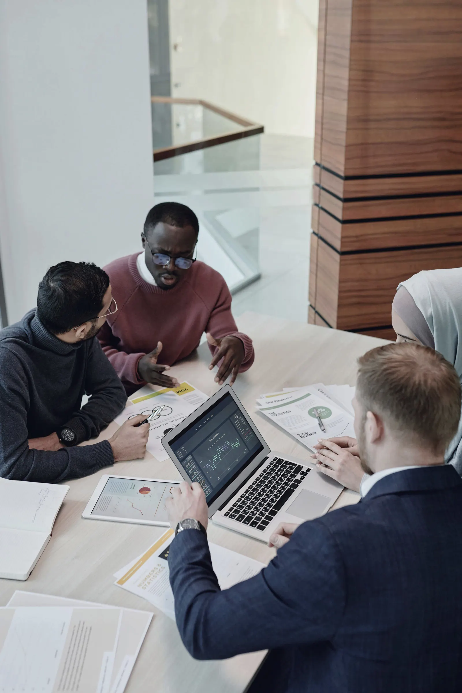 Four colleagues work at a table with laptops and papers, seen from above.