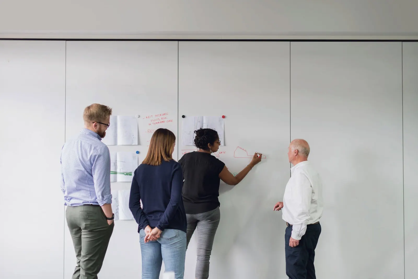 Four colleagues sort ideas on a wall of notes in a bright studio.