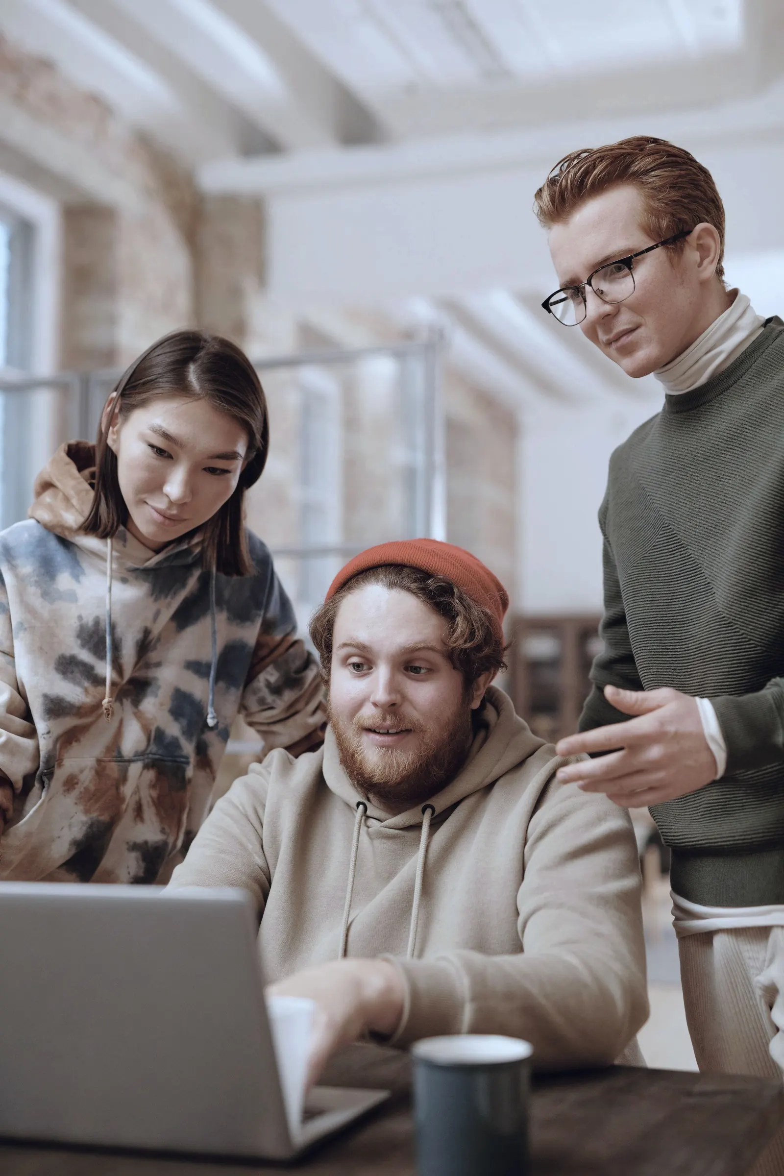 Three colleagues gather at a laptop in a brick-walled room and talk it through.