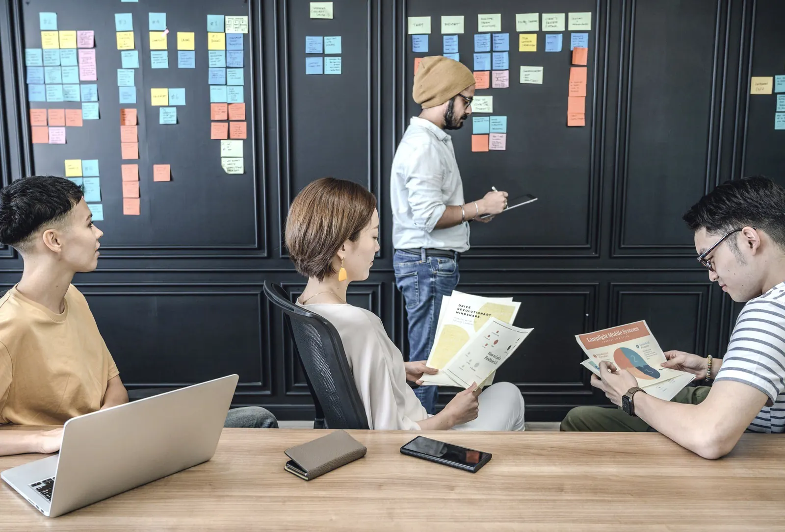 A colleague writes on a wall of notes while teammates look over documents.