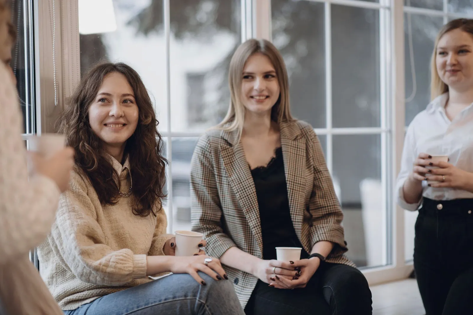 Three colleagues smile over coffee by a bright window.